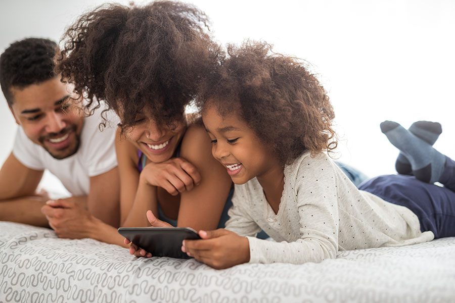 Blog - Portrait of Smiling Young Parents and Their Daughter Relaxing on the Bed While Using a Tablet