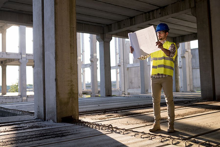 Specialized Business Insurance - View of a Contractor Standing on a New Commercial Building Construction Jobsite While Looking at Blueprints